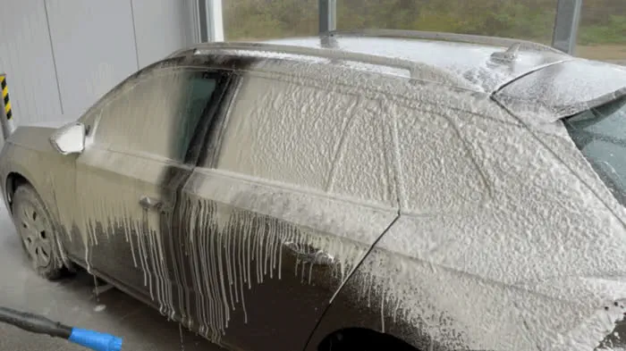 Osobní auto pokryté hustou aktivní pěnou v samoobslužném mycím boxu